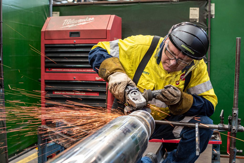 HMG team member grinding new hydraulic cylinder in the workshop.